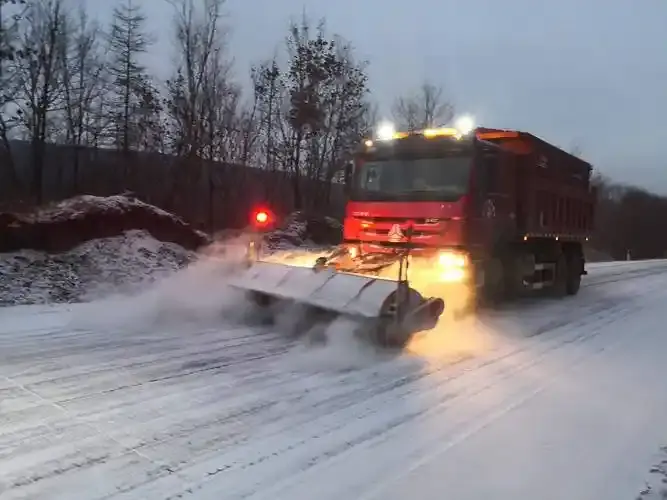 Highway winter maintenance truck spreading liquid brine guided by roadside RWIS environmental telemetry.